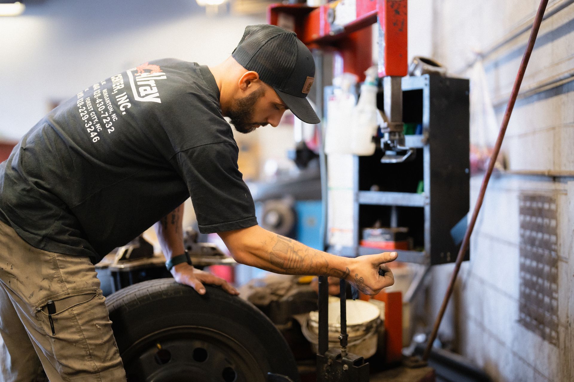 Mechanic in black cap and shirt working on a vehicle in a garage with tools and machinery nearby