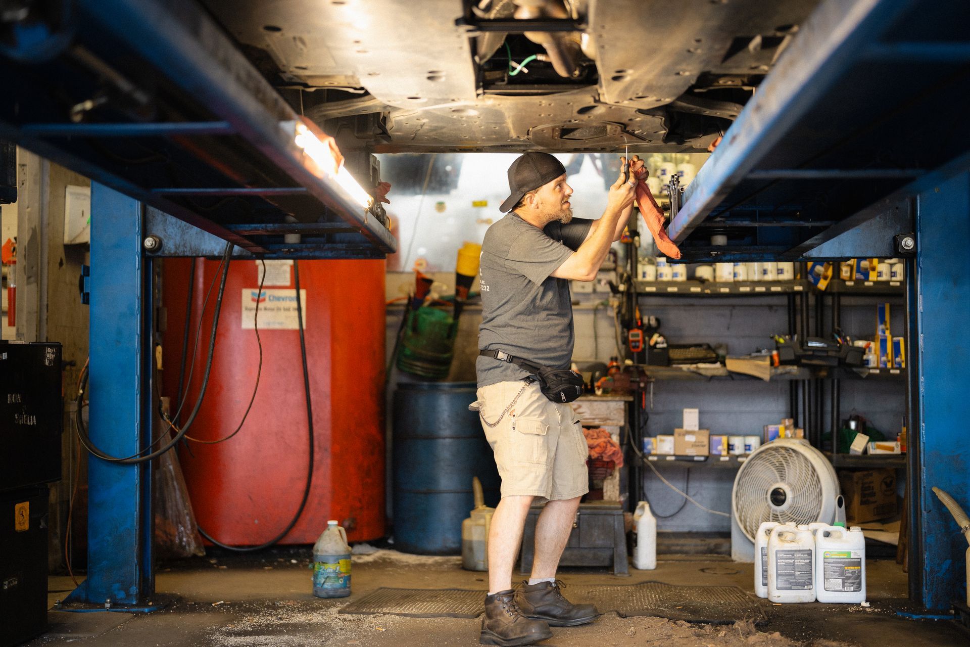 Mechanic working under a vehicle lift in a cluttered garage workshop