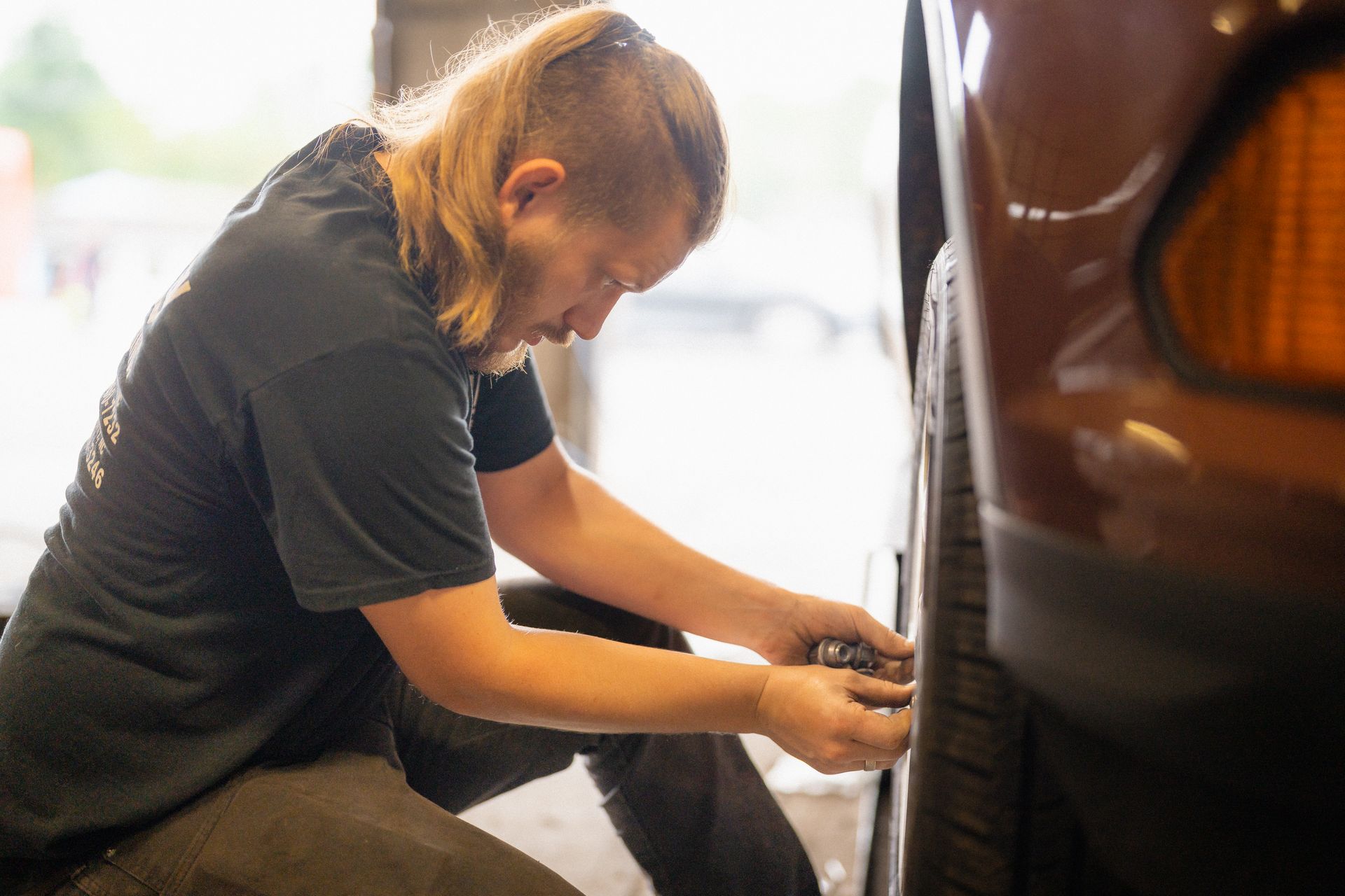 Mechanic crouching beside a car, working on the wheel area in a garage