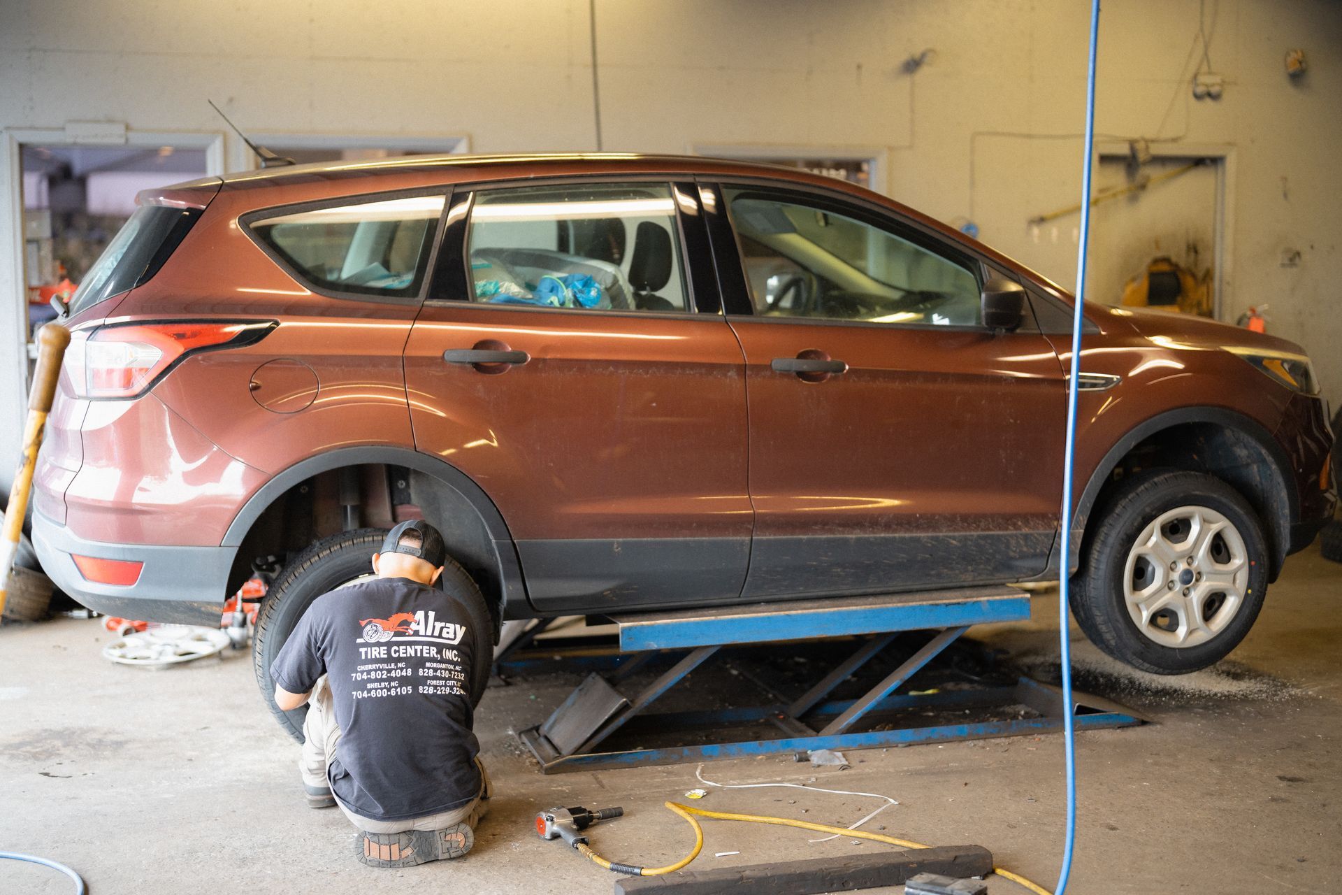 Brown SUV on a lift in a garage while a mechanic works underneath it