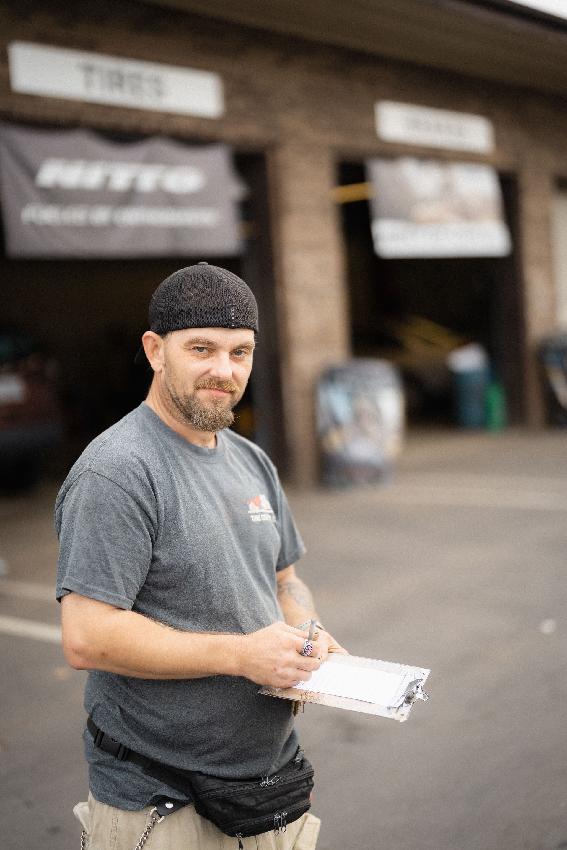 Man in black cap and gray shirt holding a clipboard outside a storefront