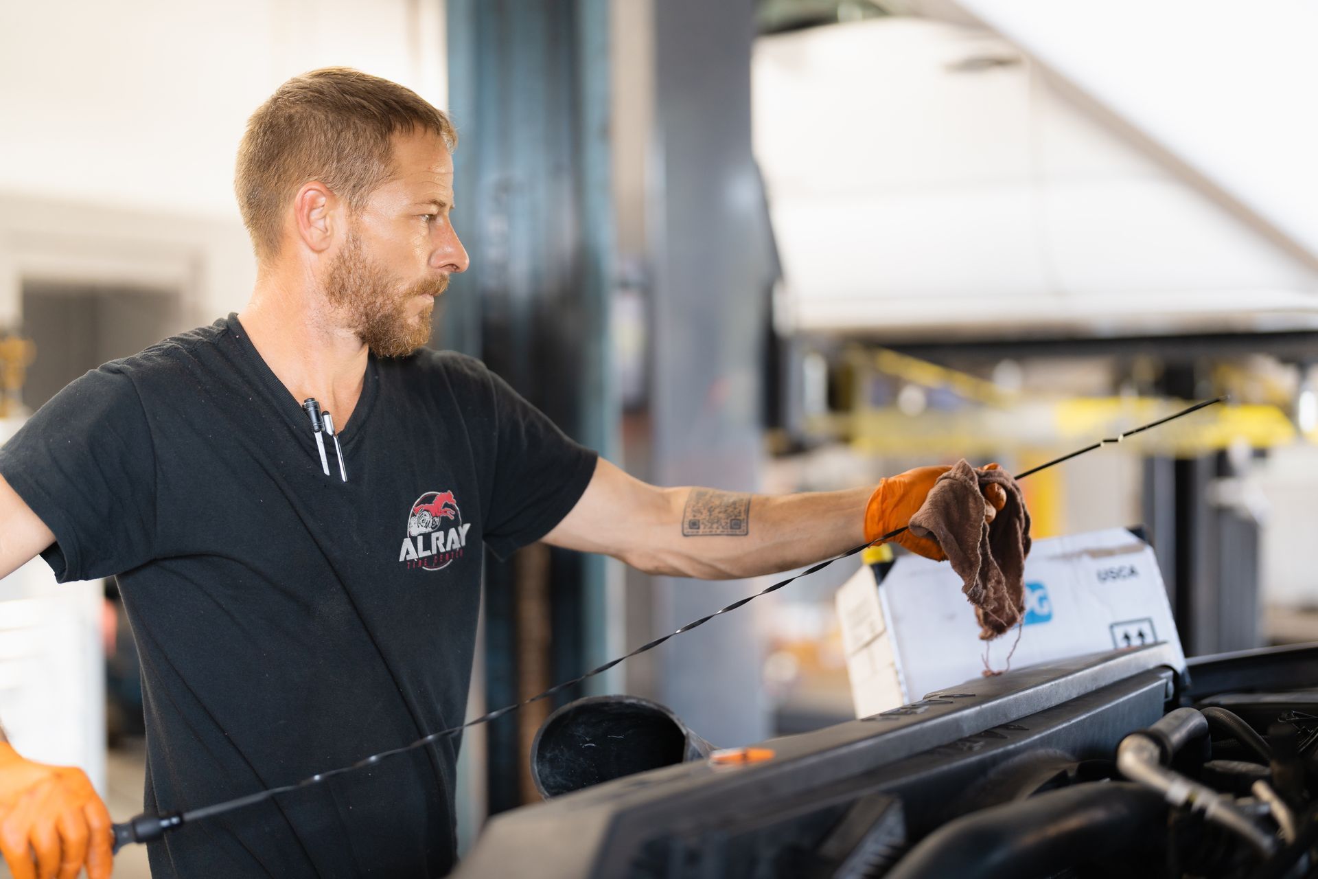 Mechanic in black shirt working on an engine in a garage, holding a tool over the open hood.