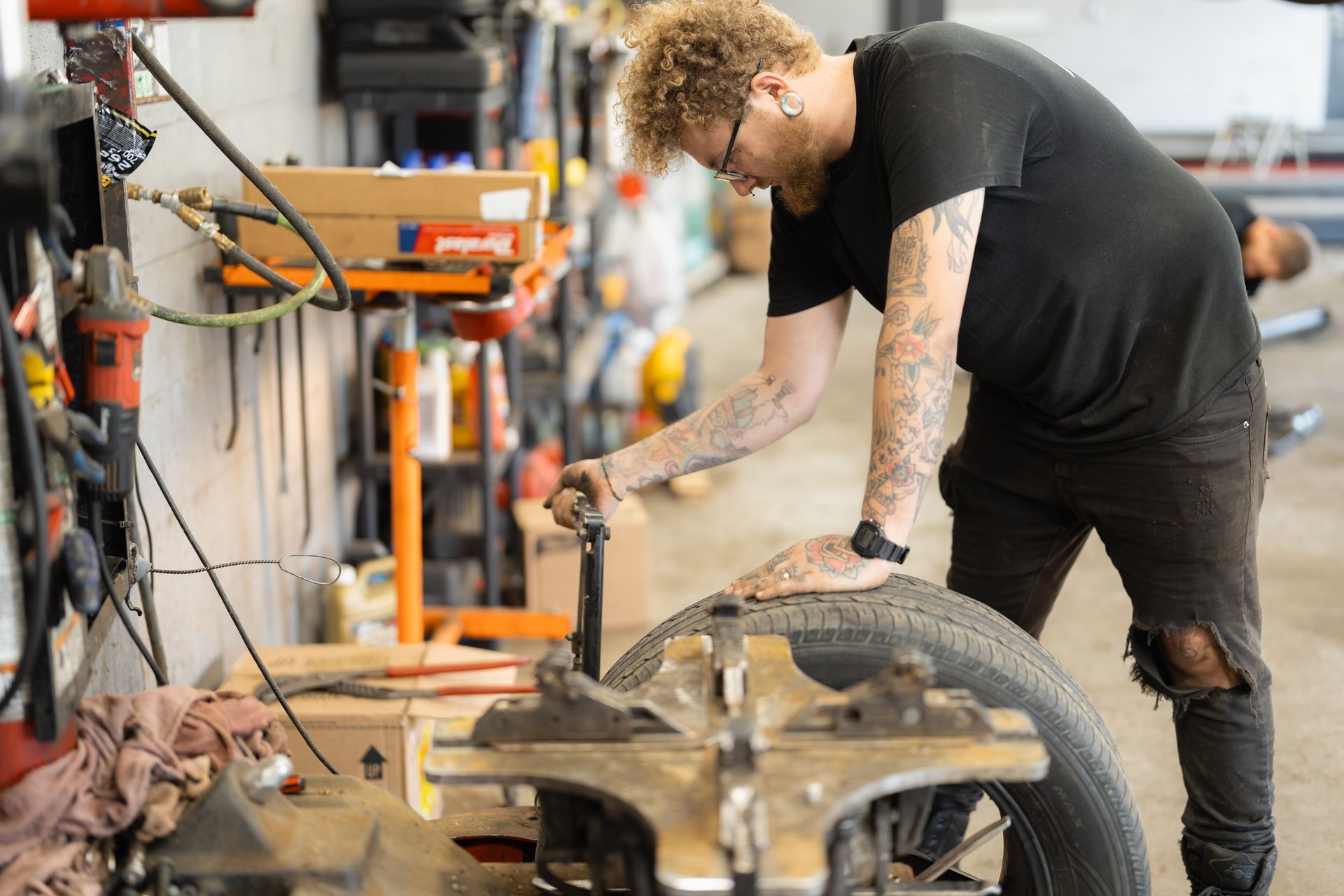 Person in black shirt bending over a motorcycle in a workshop, working with tools.