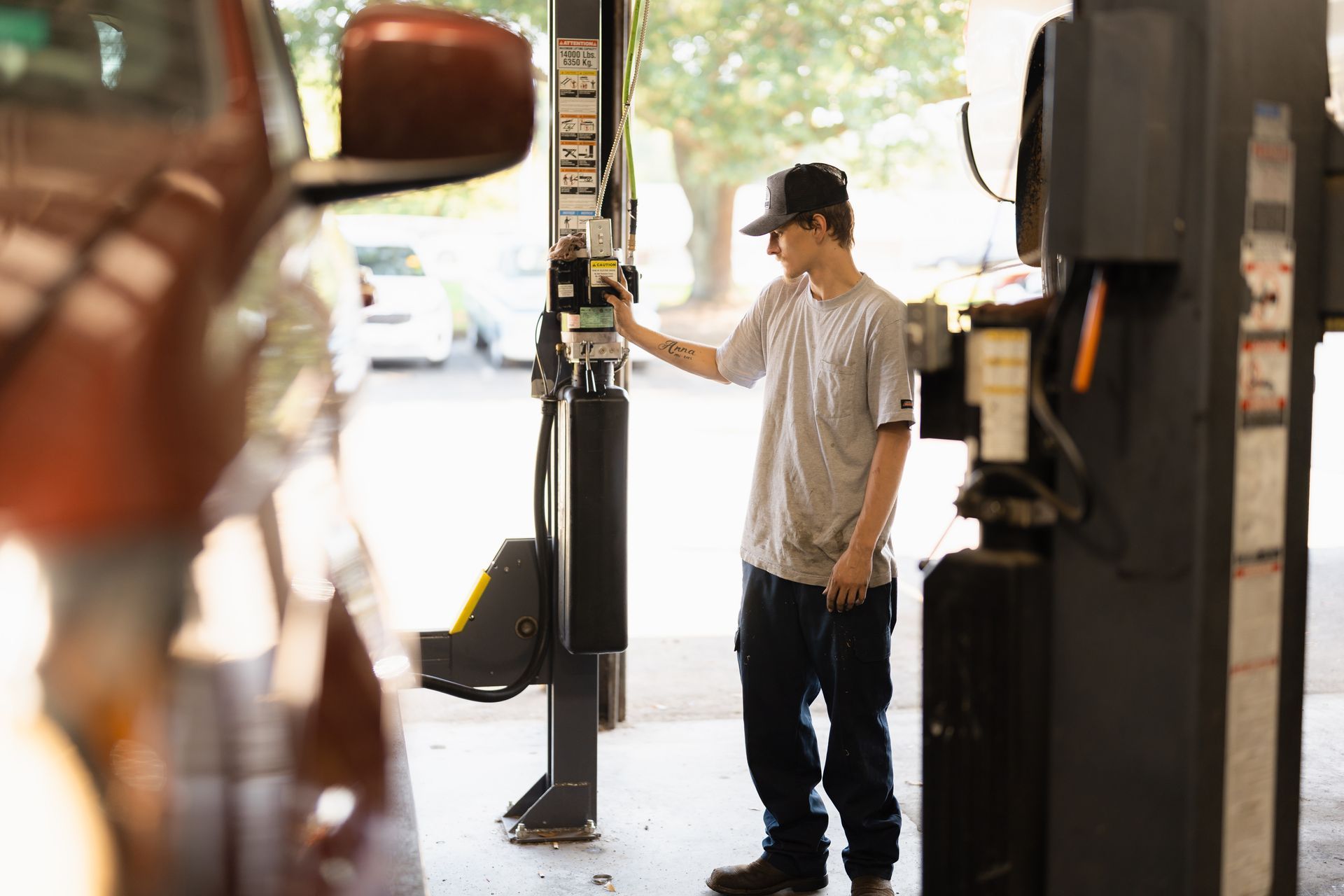 Person standing at a doorway in a garage or workshop, holding the door open near a parked vehicle.