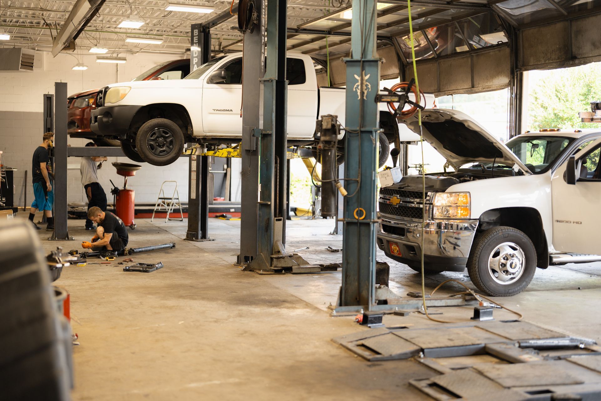 Auto repair shop with a white truck on a lift and another pickup being serviced nearby
