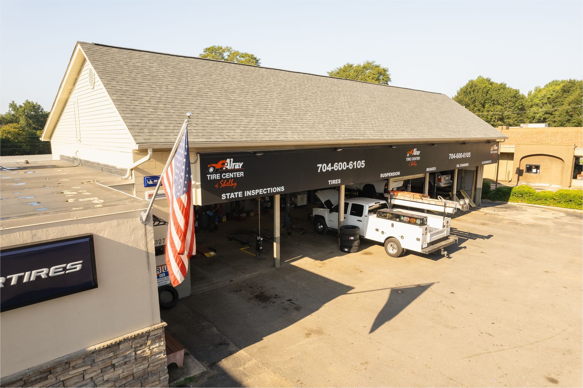 Auto service shop with open bays, white truck, and American flag at the entrance