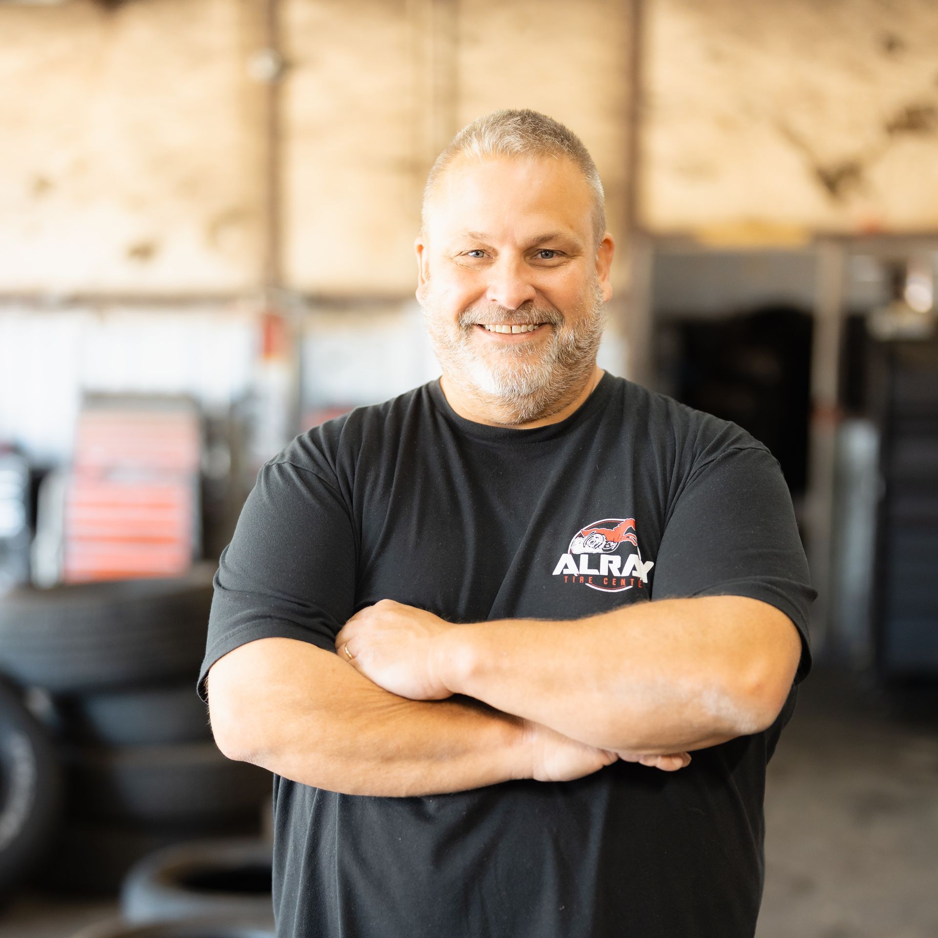 Smiling man with folded arms in a gym, wearing a black T-shirt.