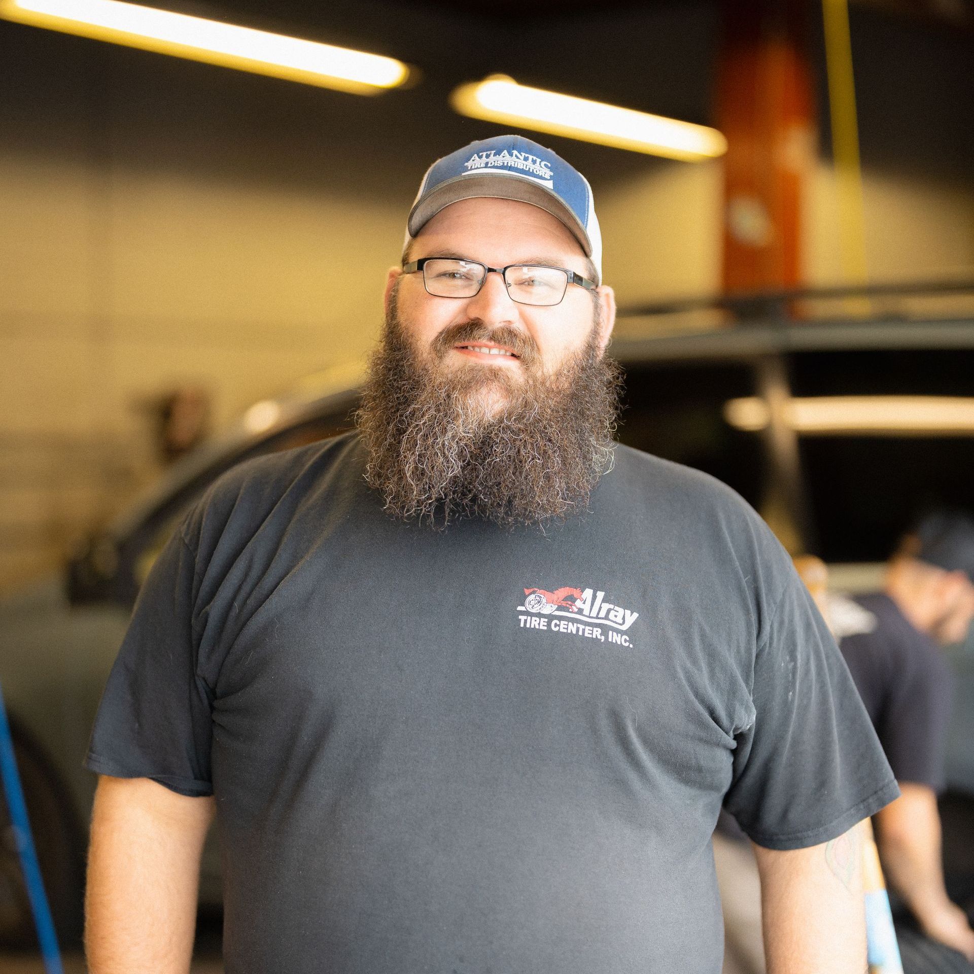 Man with a beard and glasses in a black T-shirt and blue cap standing in a workshop