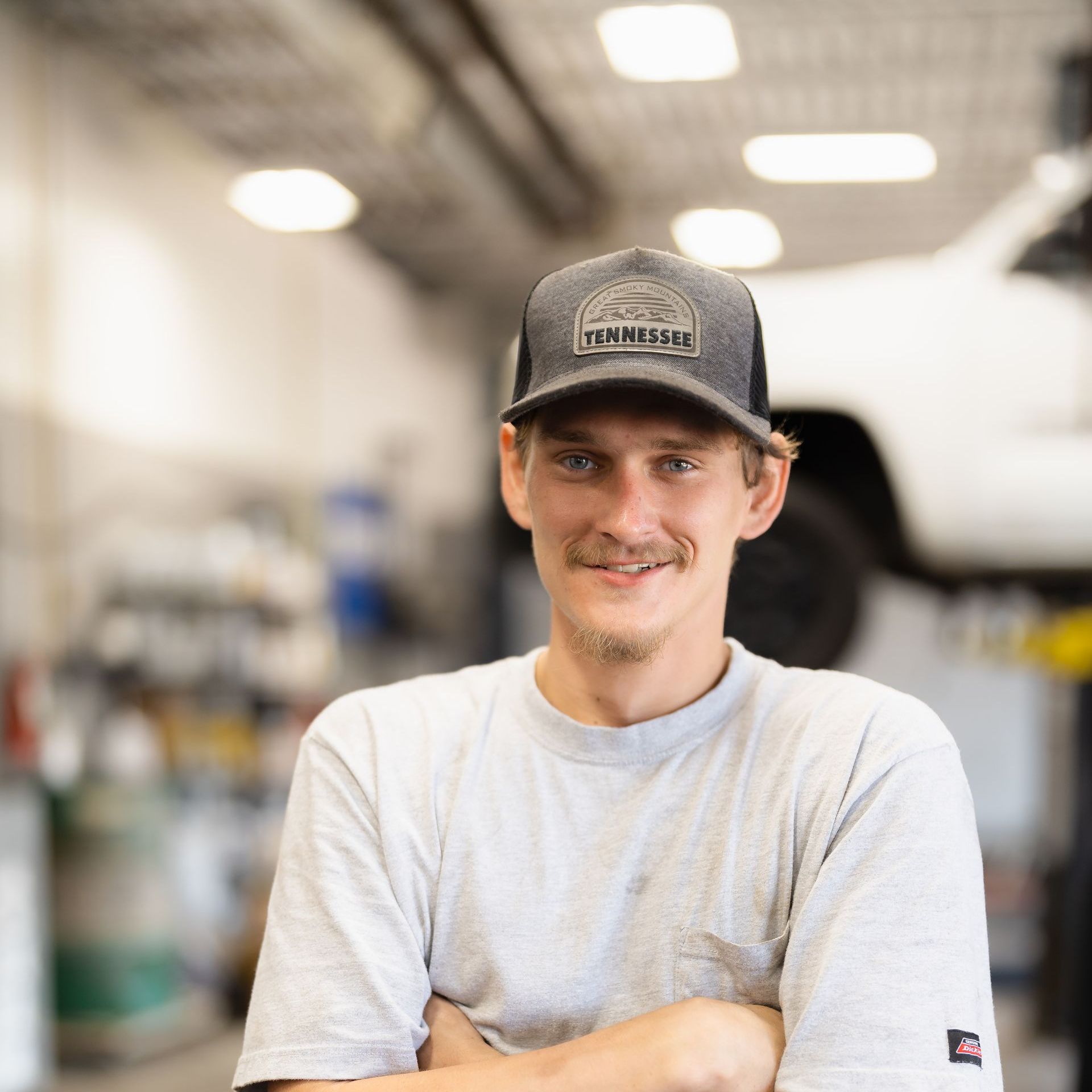 Smiling man in a gray T-shirt and cap standing in a workshop
