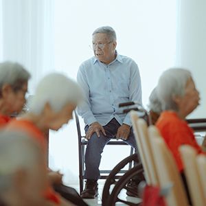 Senior man in a wheelchair speaking with seated people in a bright care facility