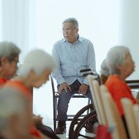 Senior man in a wheelchair speaking with seated people in a bright care facility