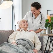 Caregiver smiling beside elderly patient resting on a couch in a bright living room