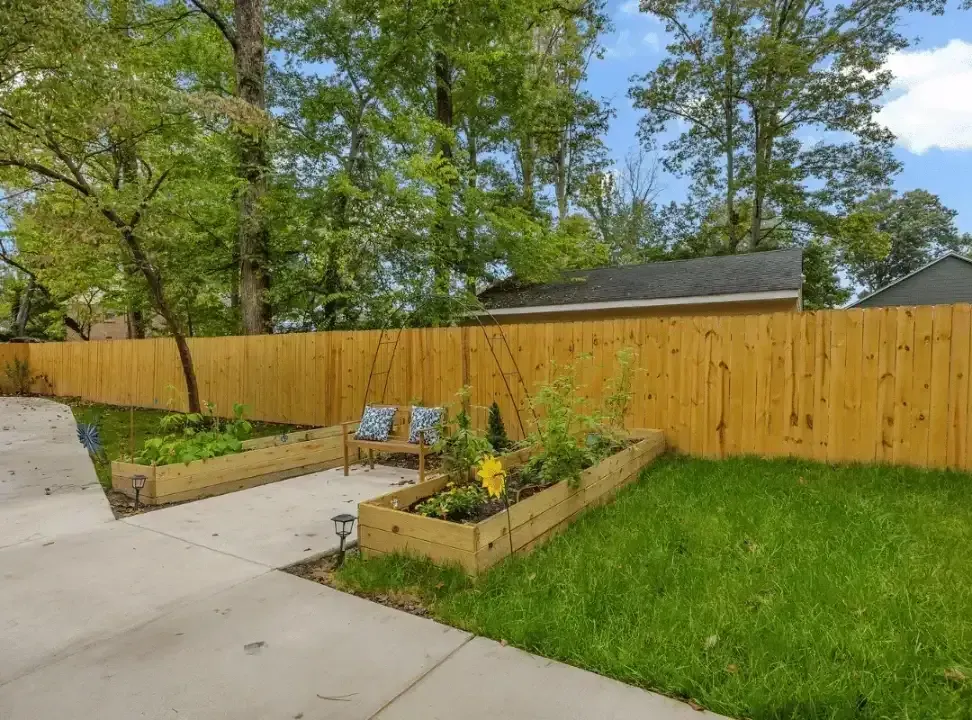 Backyard garden with raised beds, wooden fence, lawn, and concrete patio under trees