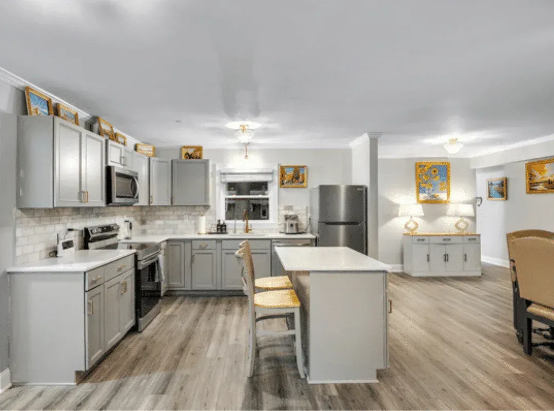 Bright modern kitchen with gray cabinets, white island, stainless appliances, and wood floors