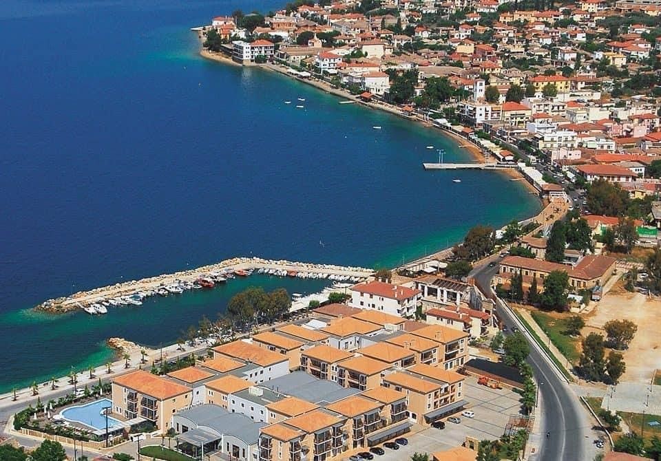 Aerial view of a coastal town with blue water, a curving shoreline, and red-roofed buildings