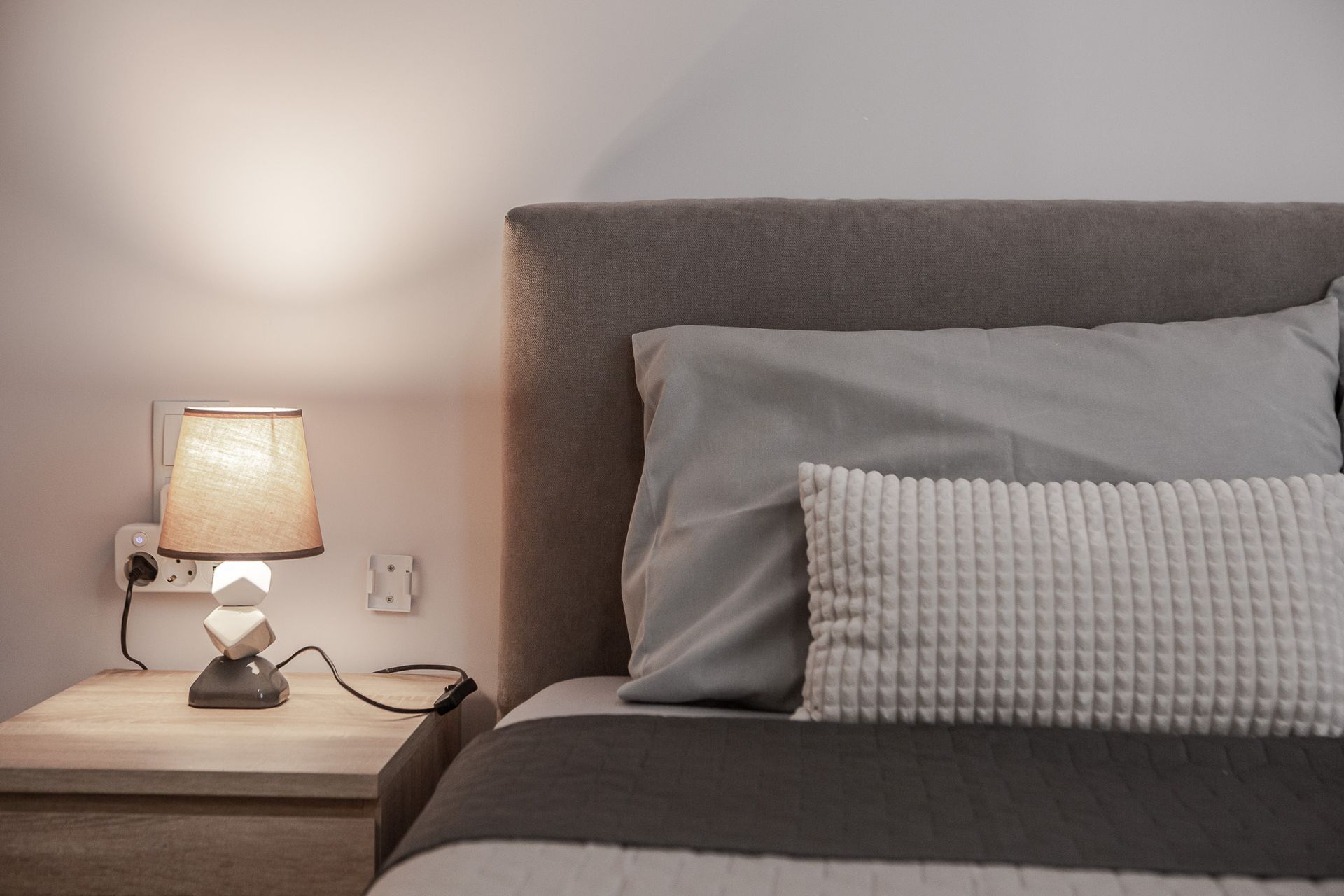 Cozy bedroom with gray bed, textured pillow, and lit bedside lamp on a wooden nightstand