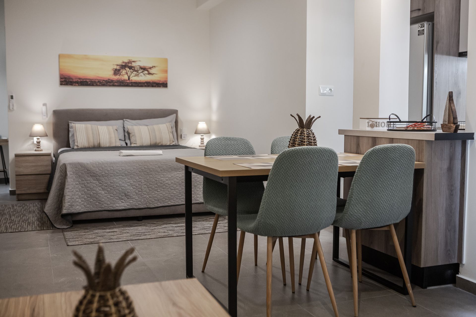 Modern bedroom with a king bed, gray seating area, and small dining table in a neutral-toned room