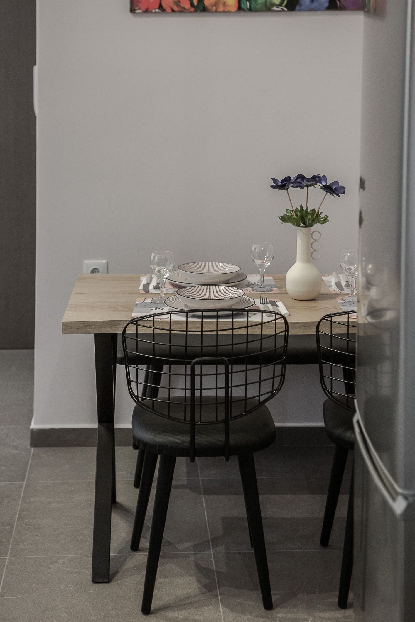 Small dining nook with a wooden table, black chairs, and a vase of blue flowers against a gray wall.