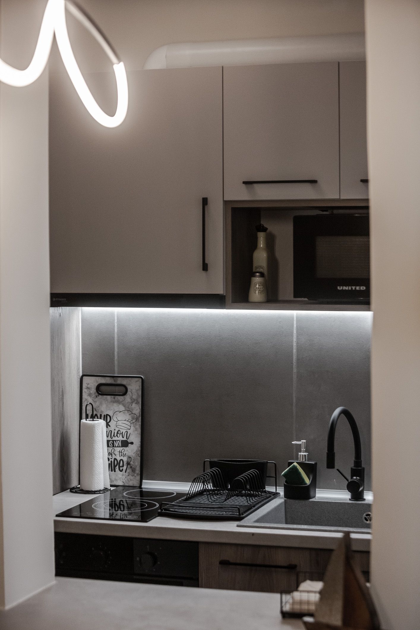 Modern kitchen with gray cabinets, under-cabinet lighting, stove, sink, and countertop accessories