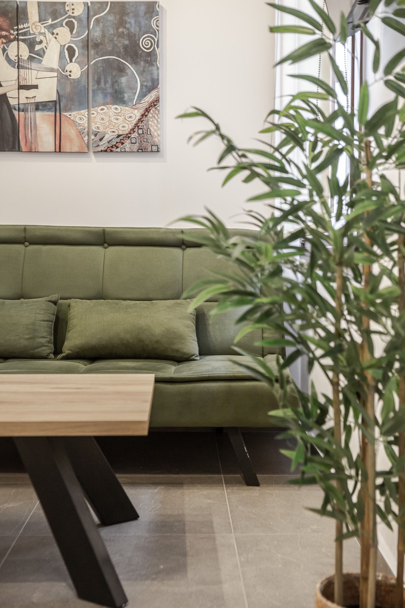 Modern living room with green sofa, wooden coffee table, wall art, and tall potted plant