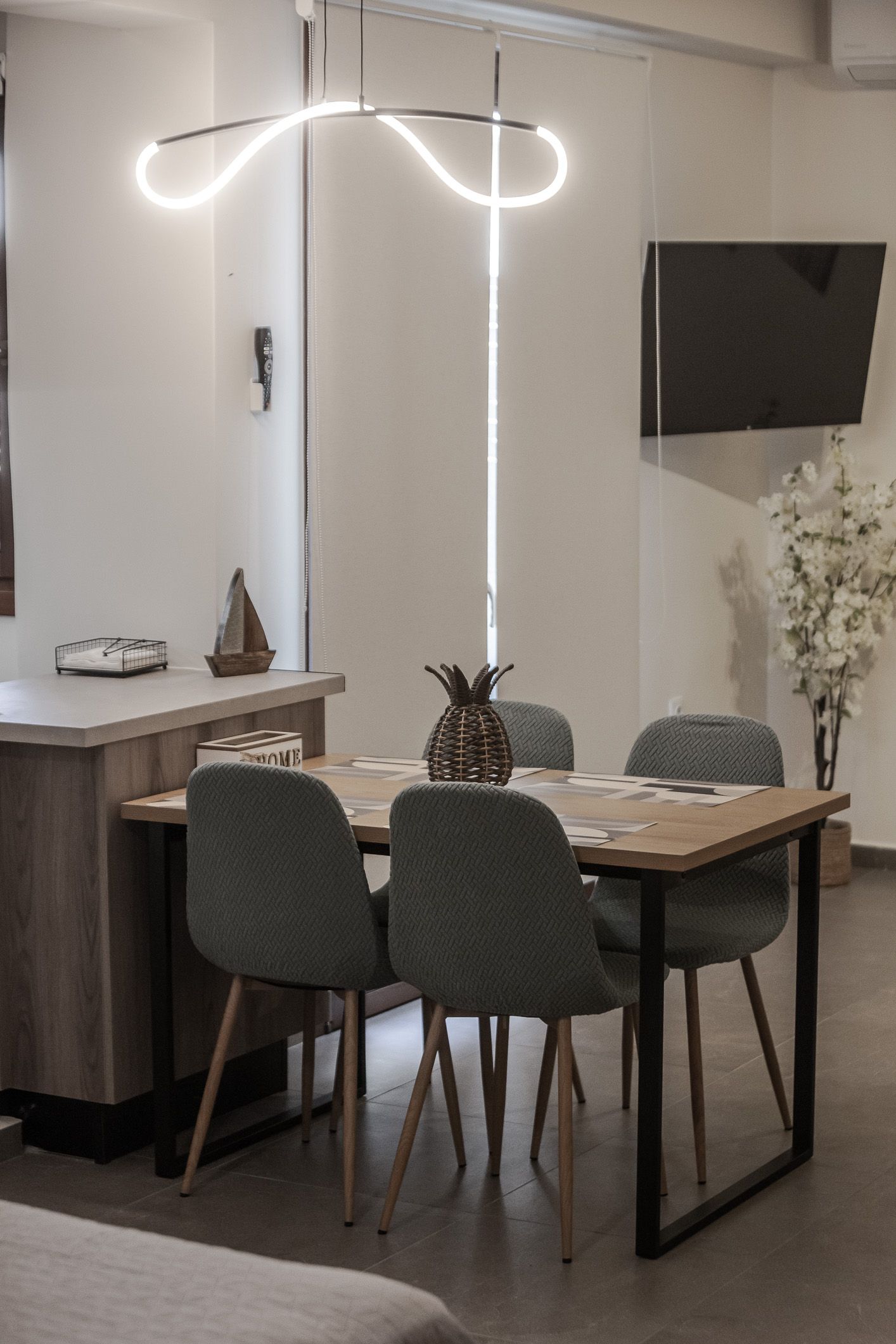 Modern dining area with a lit pendant light, table, chairs, and wall-mounted TV