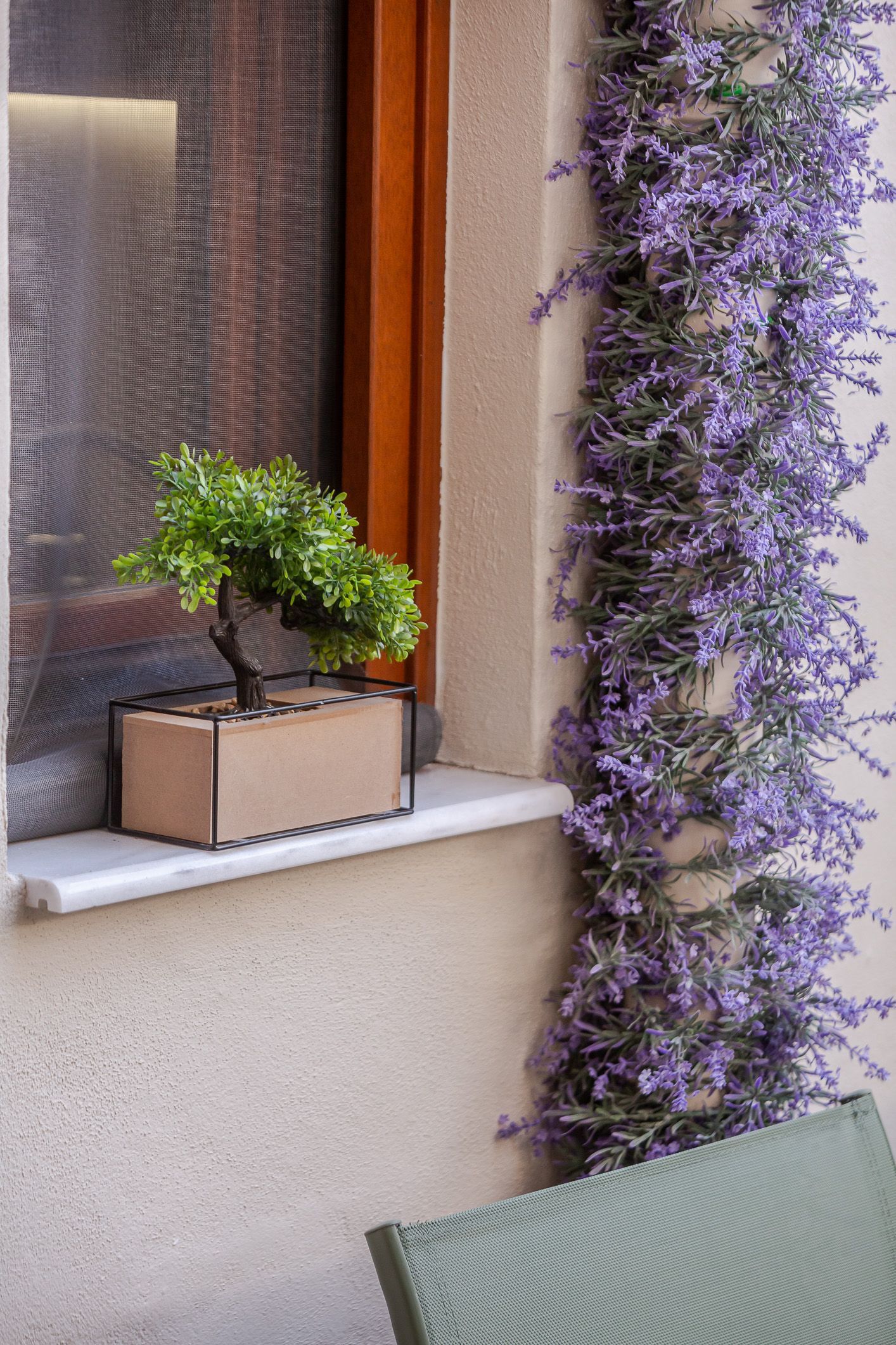 Small potted tree on a windowsill beside a lavender-flowered vine on a stucco wall