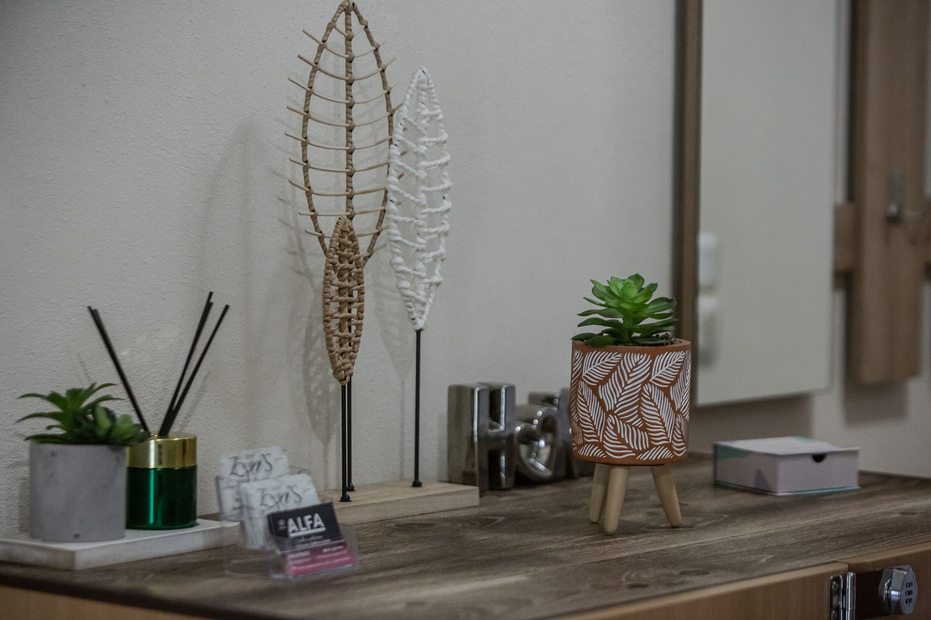 Decorative shelf with potted plants, reed diffusers, and metal leaf sculptures on a wooden surface