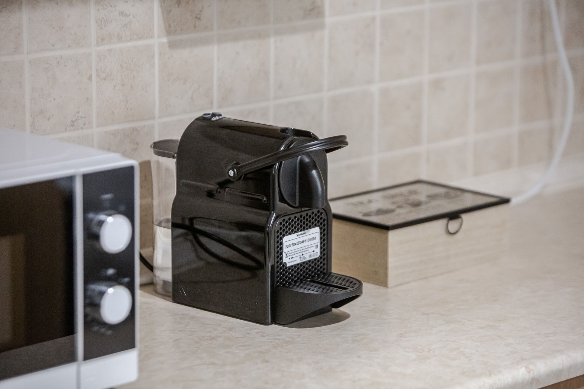 Black coffee machine on a kitchen counter beside a microwave and a small box.