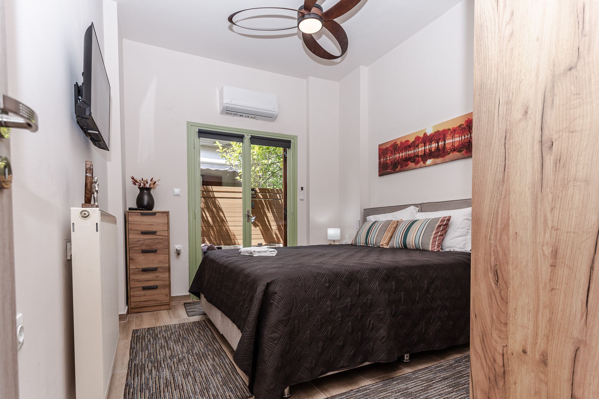 Small bedroom with a black bedspread, dresser, wall TV, and sliding glass door to a balcony.