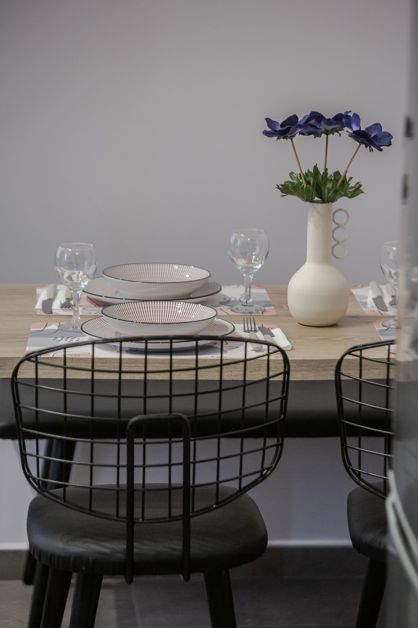 Set dining table with plates, glasses, and a vase of purple flowers beside black chairs