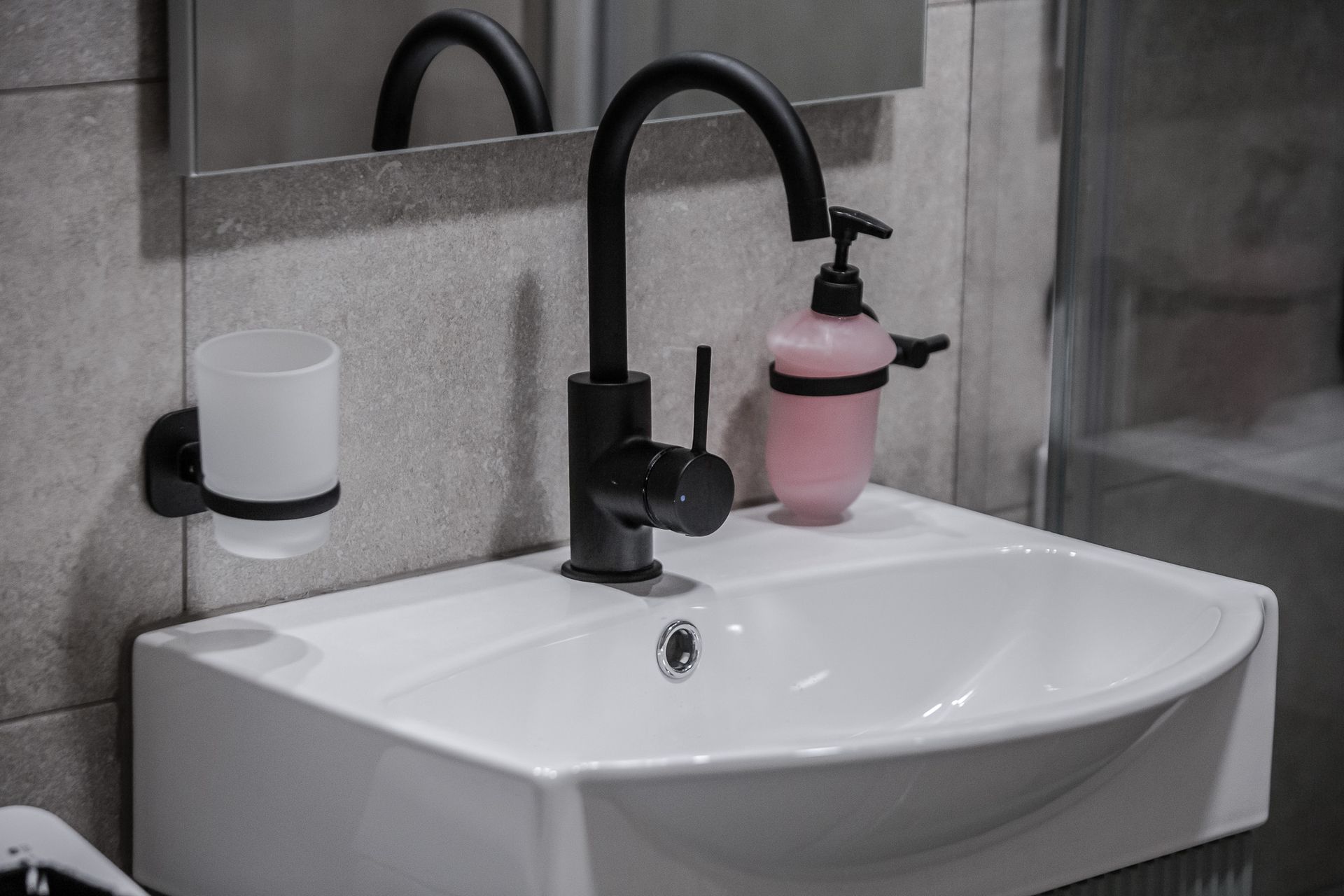 Bathroom sink with black faucet, white basin, and a pink soap dispenser on the counter.