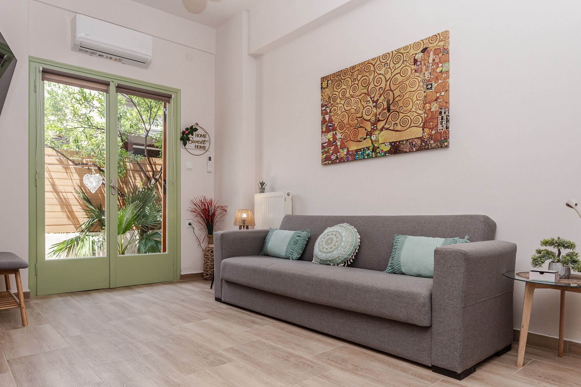 Bright living room with a gray sofa, green French doors, and wall art on white walls.