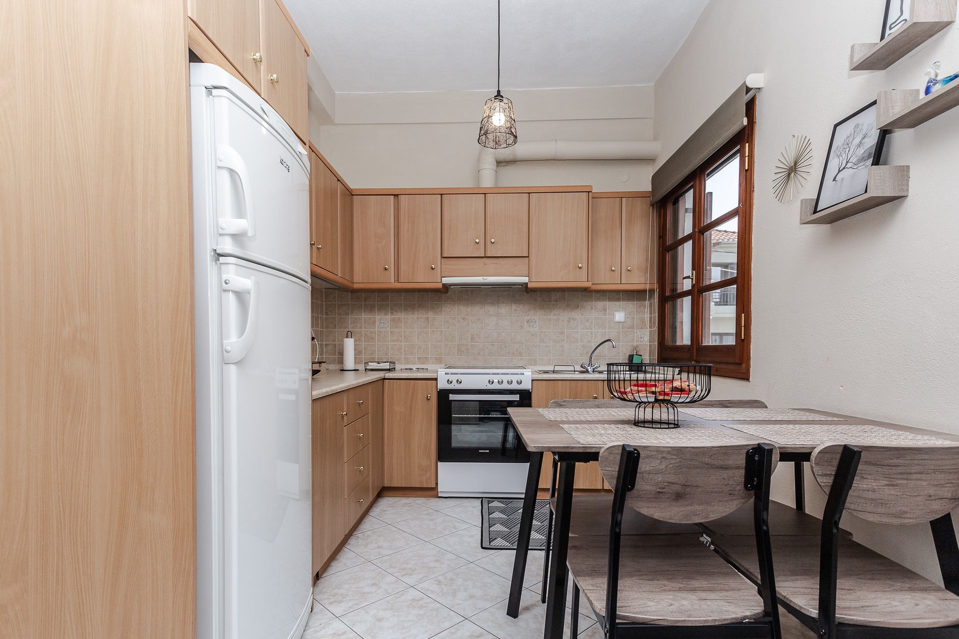Narrow kitchen with wood cabinets, white appliances, and a small dining table by a window.