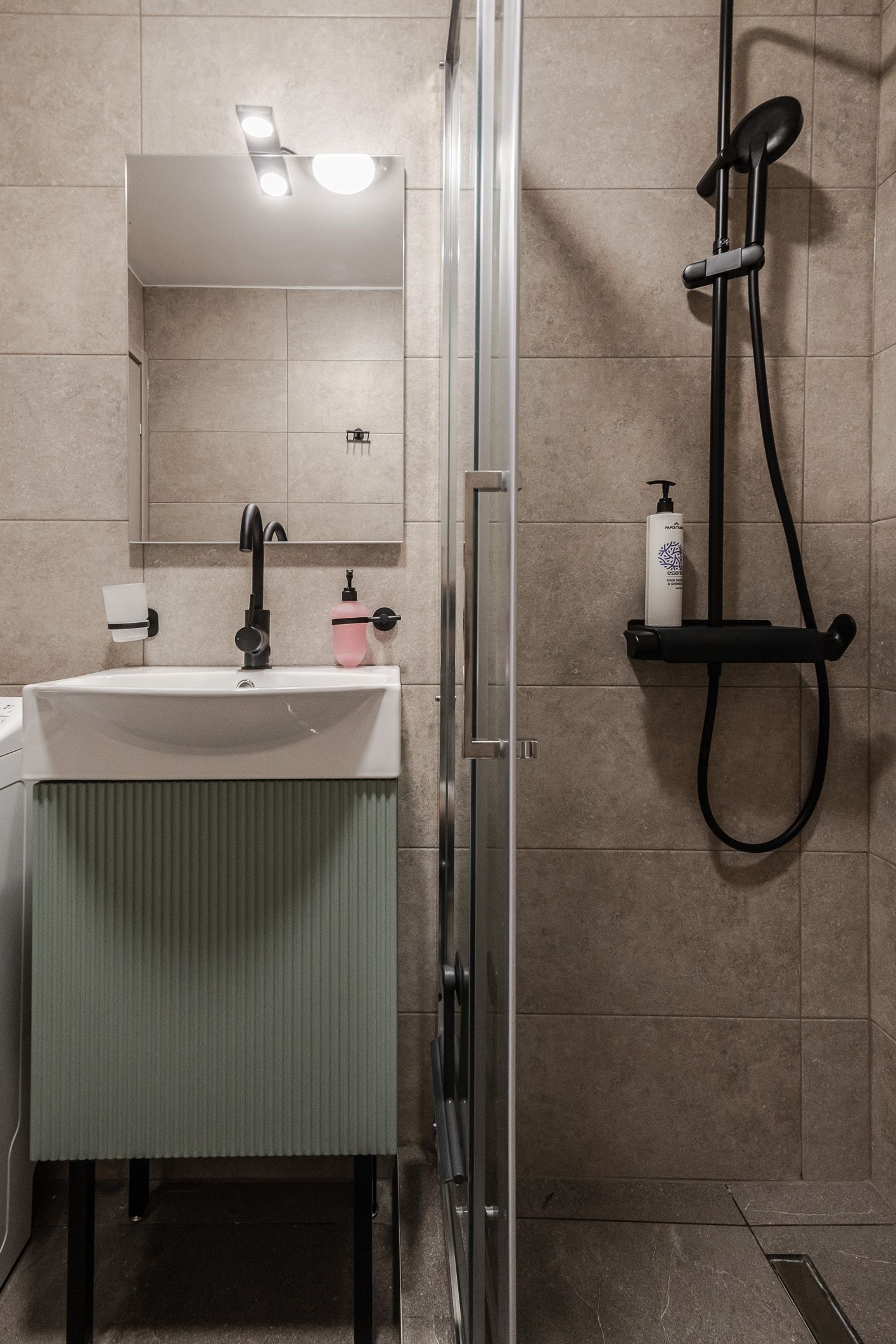 Small bathroom with sink and mirror on the left and a tiled shower with grab bar on the right.