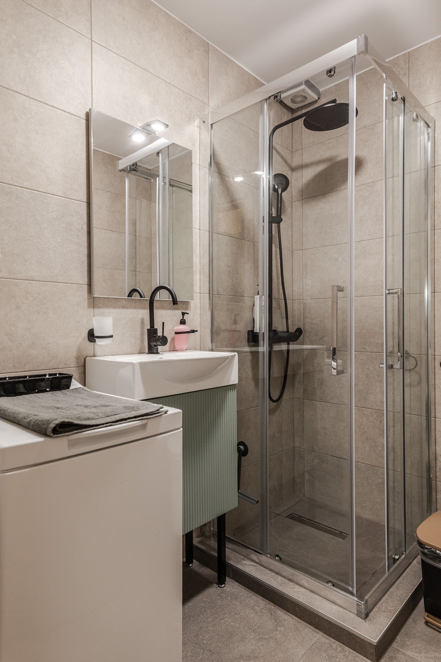 Small bathroom with a sink, mirror, and glass shower stall with beige tile walls