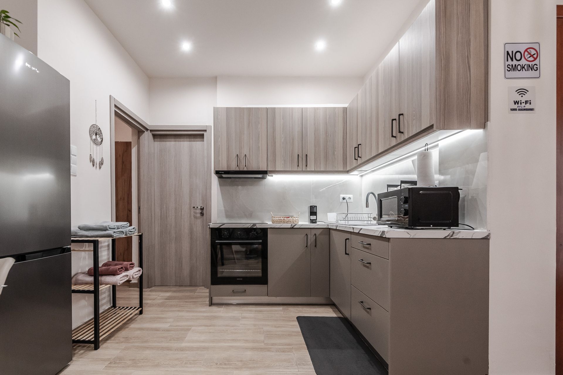 Modern kitchen with wood cabinets, gray countertops, built-in oven, and open shelving under bright lighting