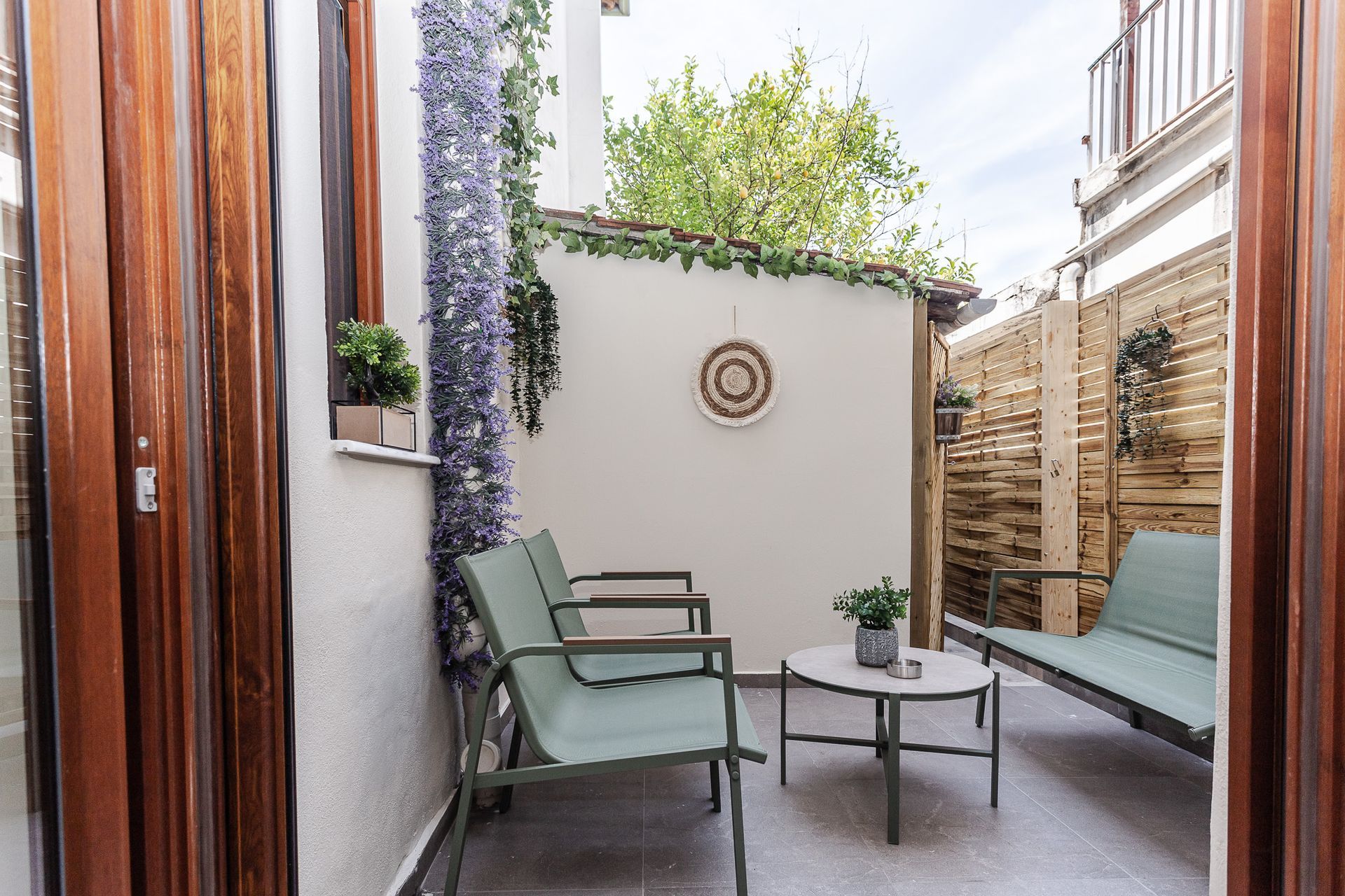 Narrow patio with mint lounge chairs, small table, and potted greenery between wooden walls