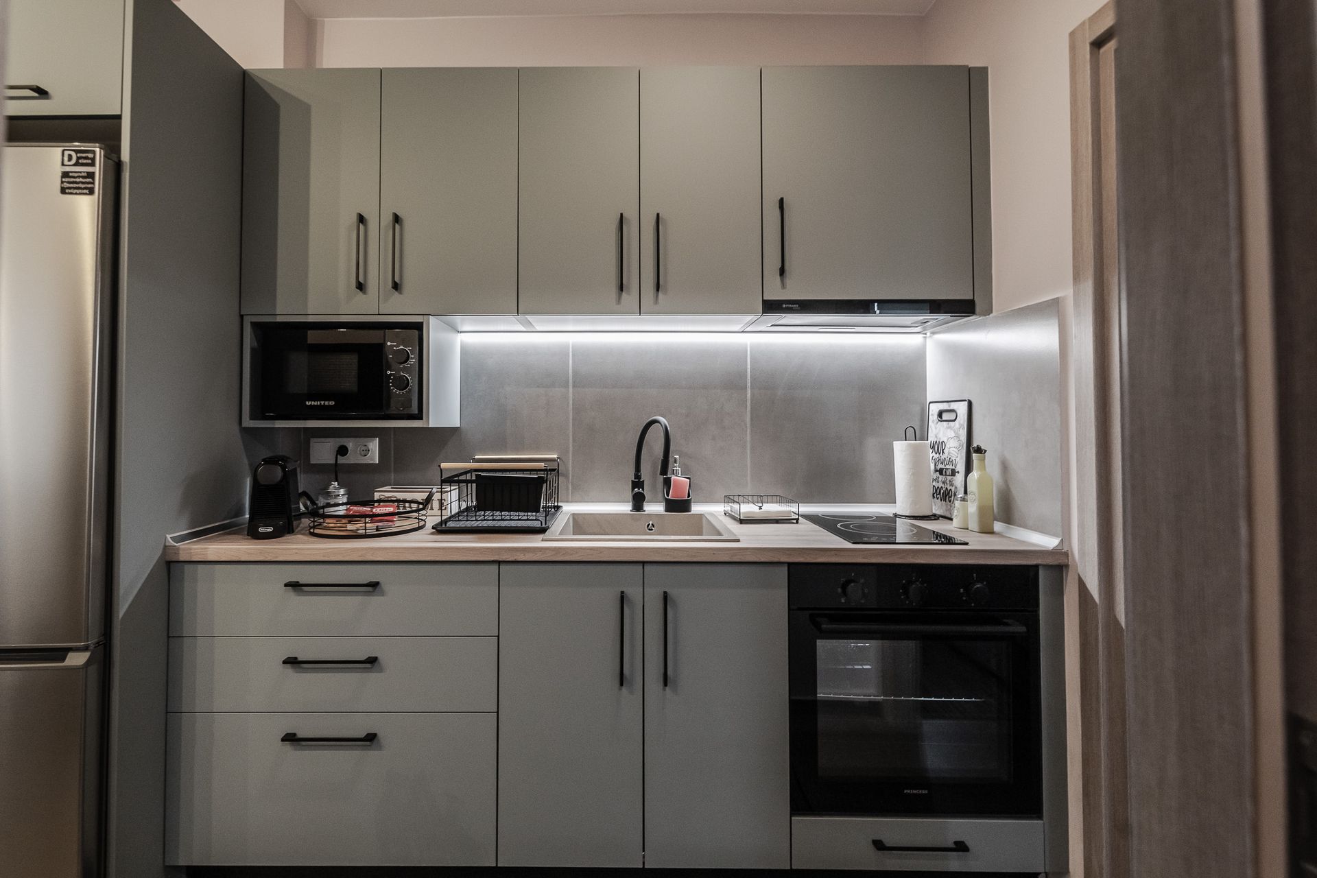 Compact gray kitchen with cabinets, microwave, sink, stove, and under-cabinet lighting