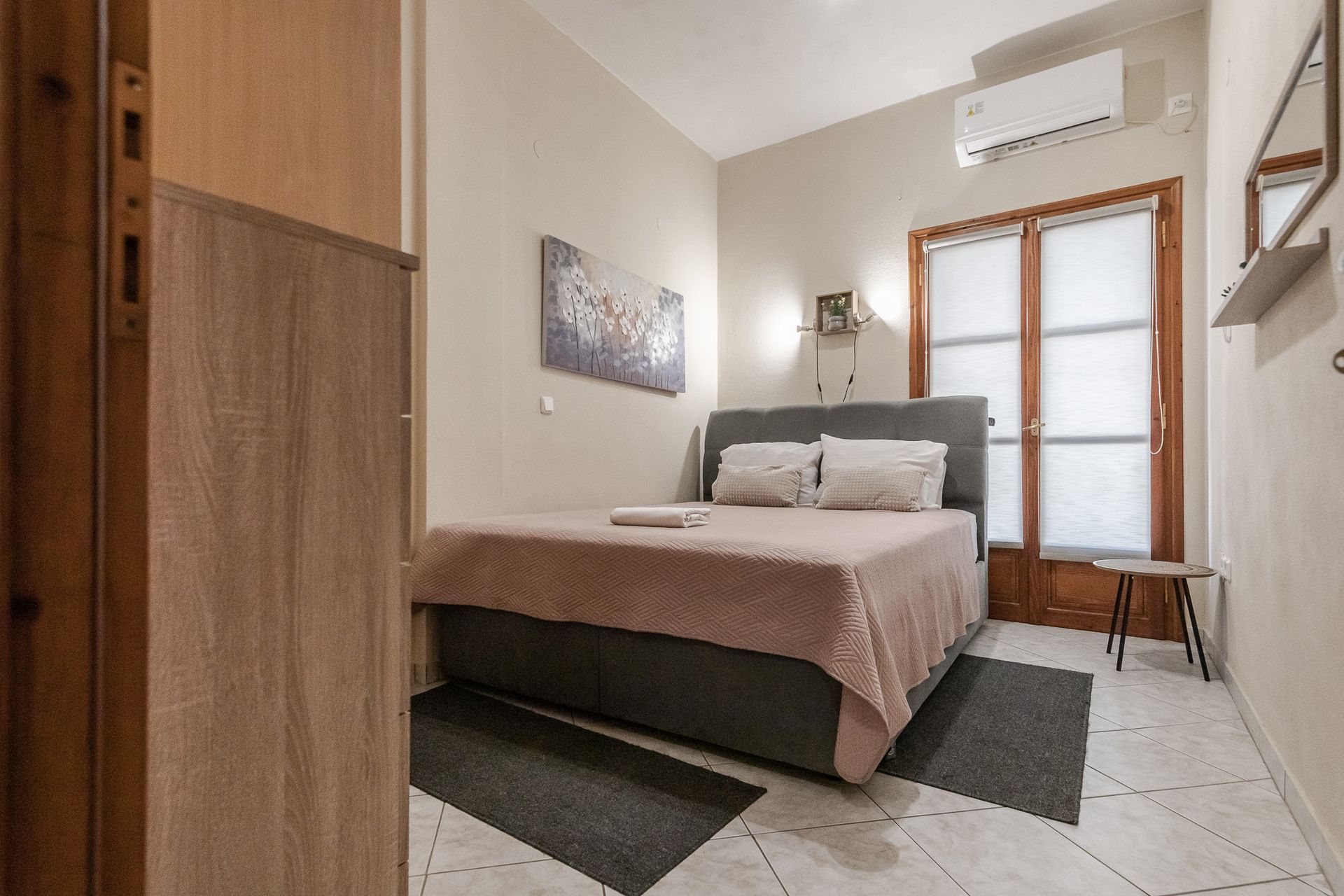 Small bedroom with a bed, wardrobe, wall art, and a windowed door in a bright, minimalist room