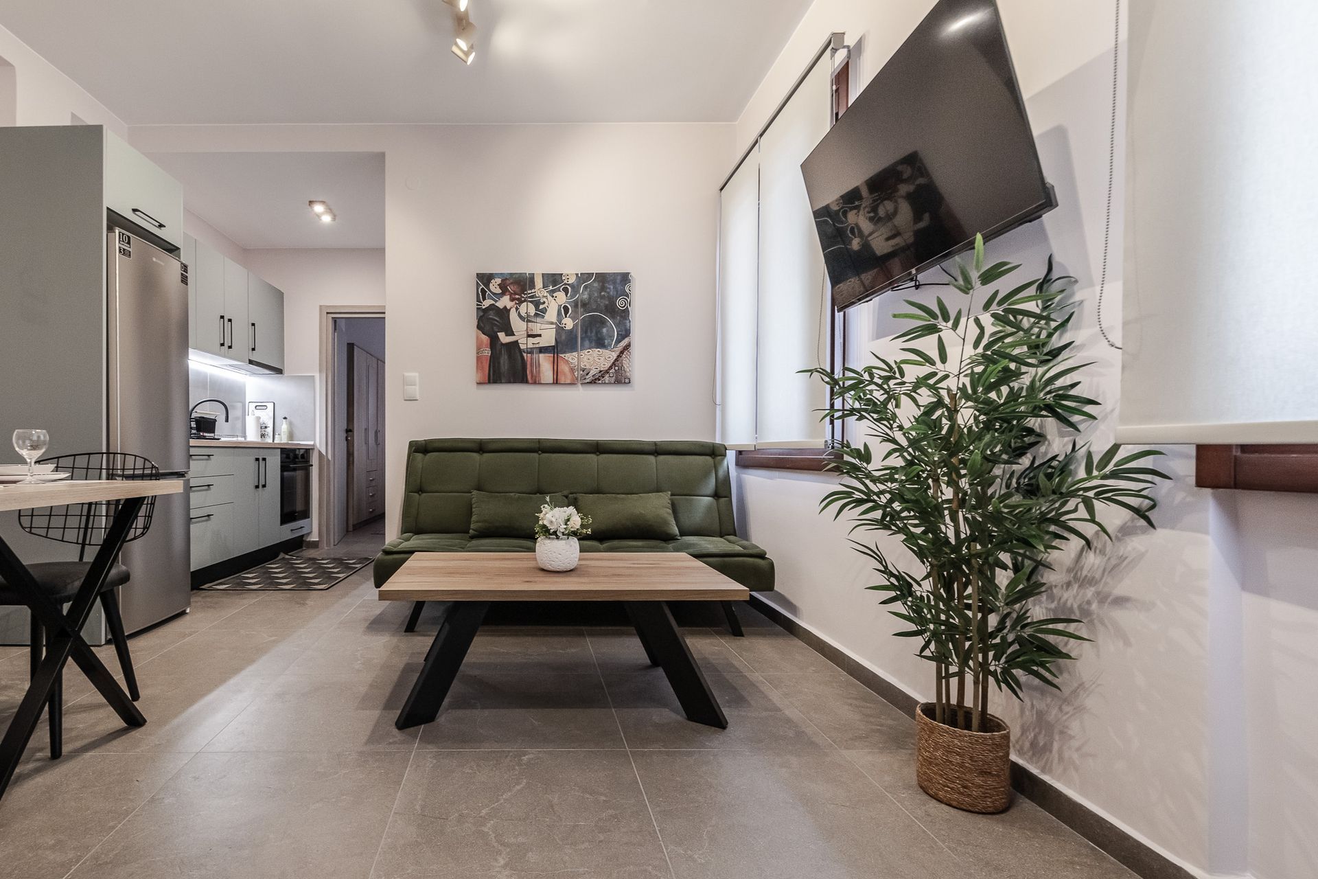 Bright modern living room with green sofa, coffee table, wall-mounted TV, and potted plant near a bright window.