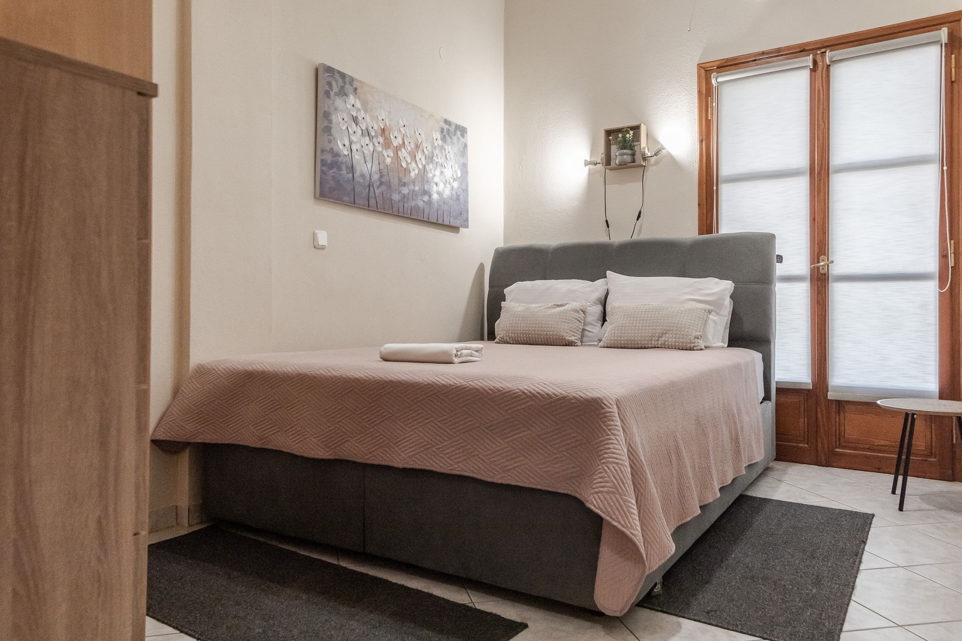 Cozy bedroom with a neatly made bed, wall art, wardrobe, and a windowed door.