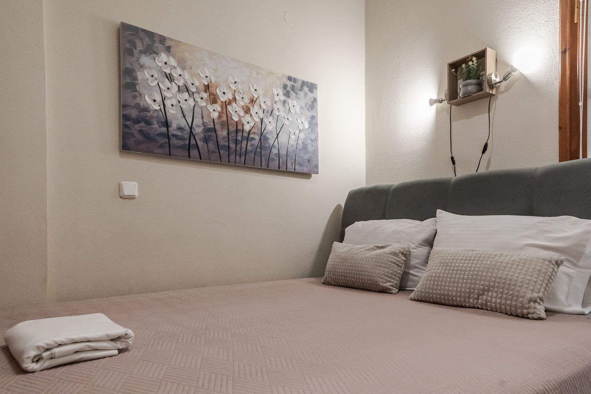 Neat bedroom with beige bed, gray headboard, folded towels, and a floral wall painting