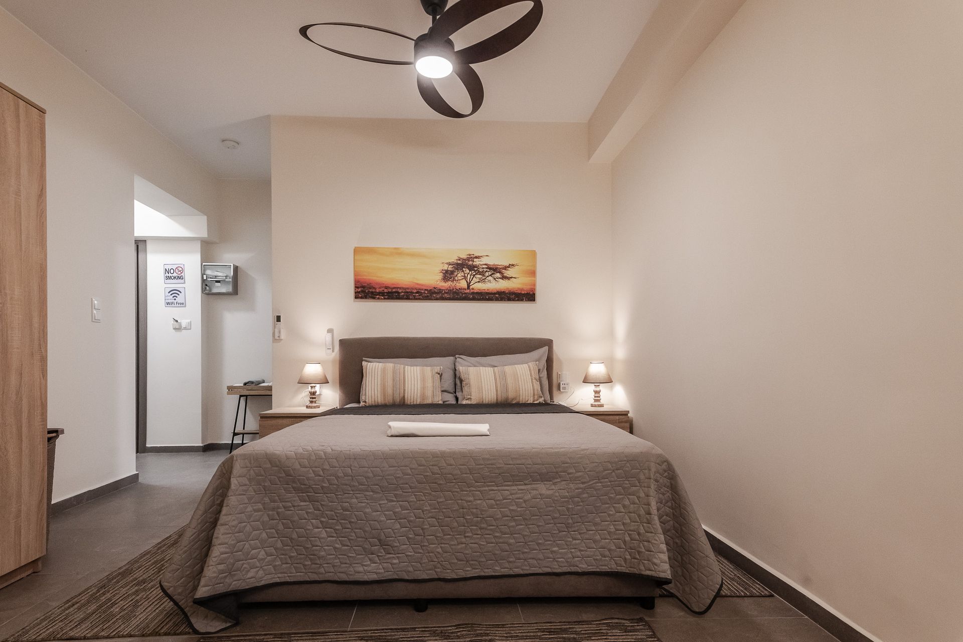Modern bedroom with a neatly made bed, bedside lamps, wall art, and a ceiling fan