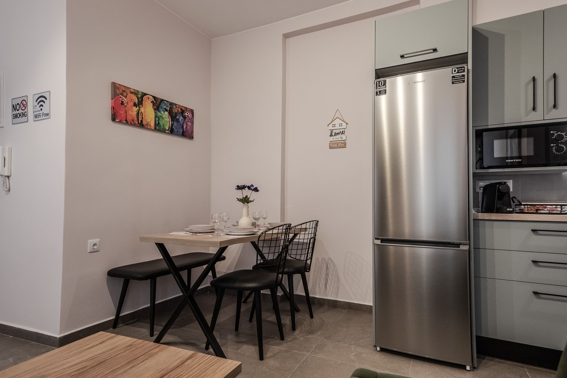 Small kitchen with dining table, black chairs, stainless steel refrigerator, and pale cabinets.