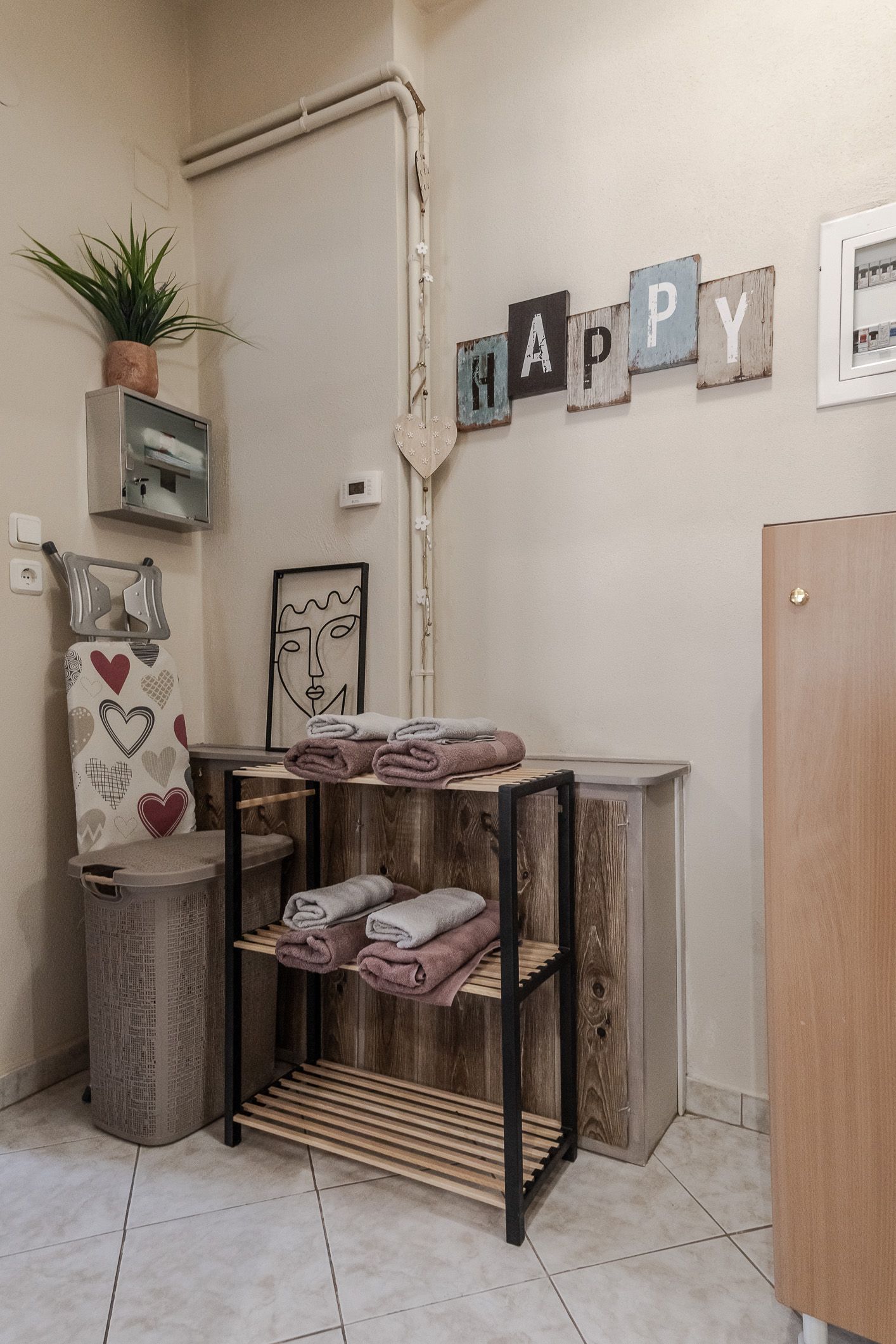 Small cozy room with a shelf, towels, plant, and wall decor spelling “HAPPY.”