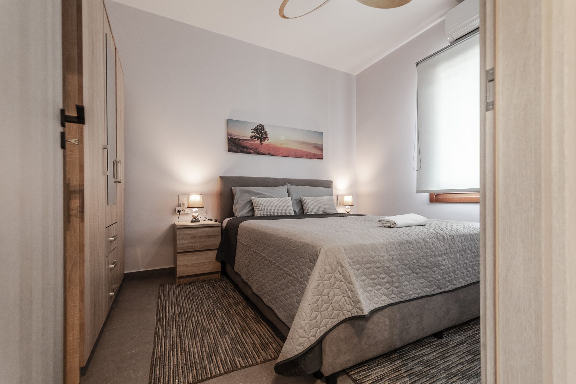 Bright bedroom with a neatly made bed, two bedside lamps, and a window with blinds