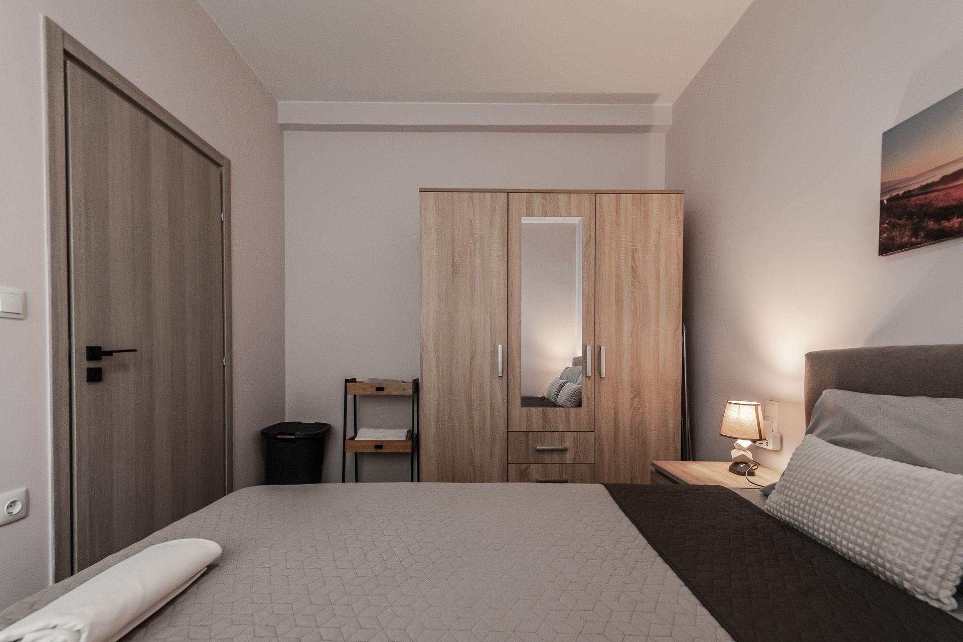 Minimal bedroom with a bed, wardrobe, nightstand lamp, and wooden door in soft neutral tones