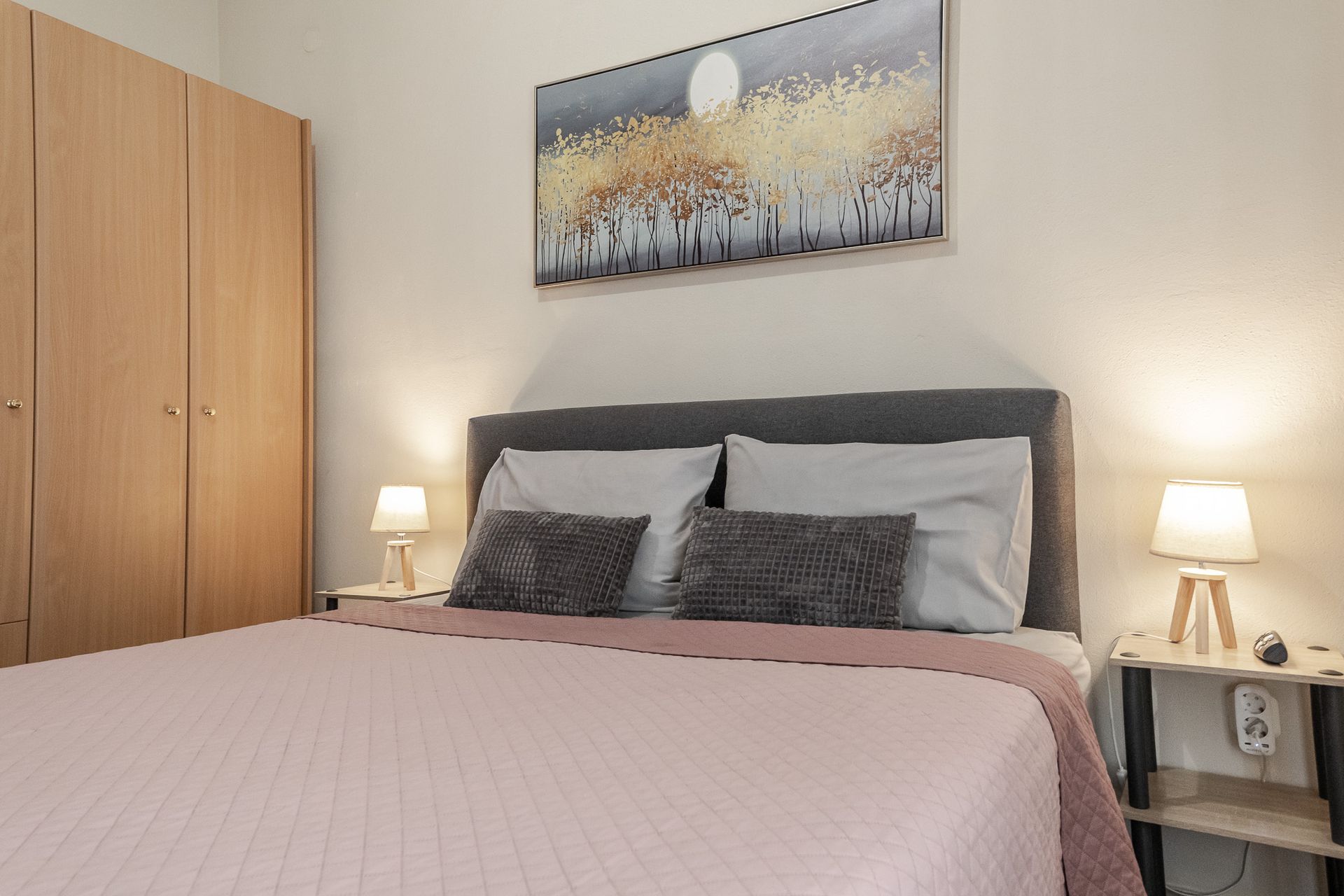 Cozy bedroom with a neatly made bed, bedside lamps, wardrobe, and framed wall art.