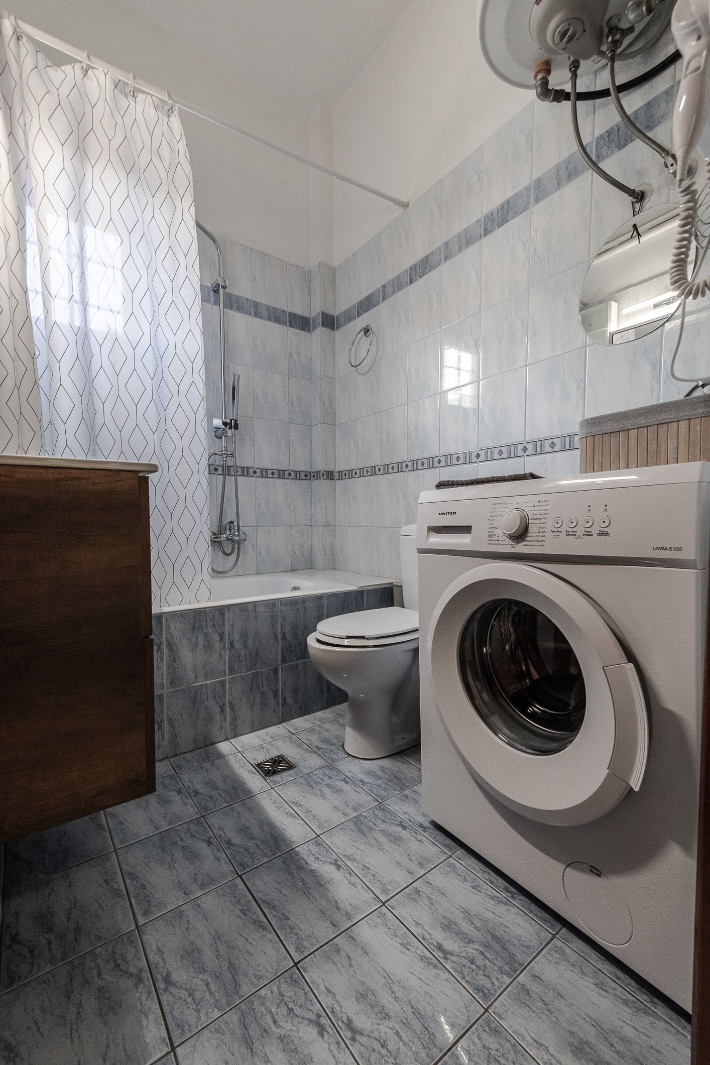 Small bathroom with washing machine, toilet, tiled walls, shower curtain, and gray floor.