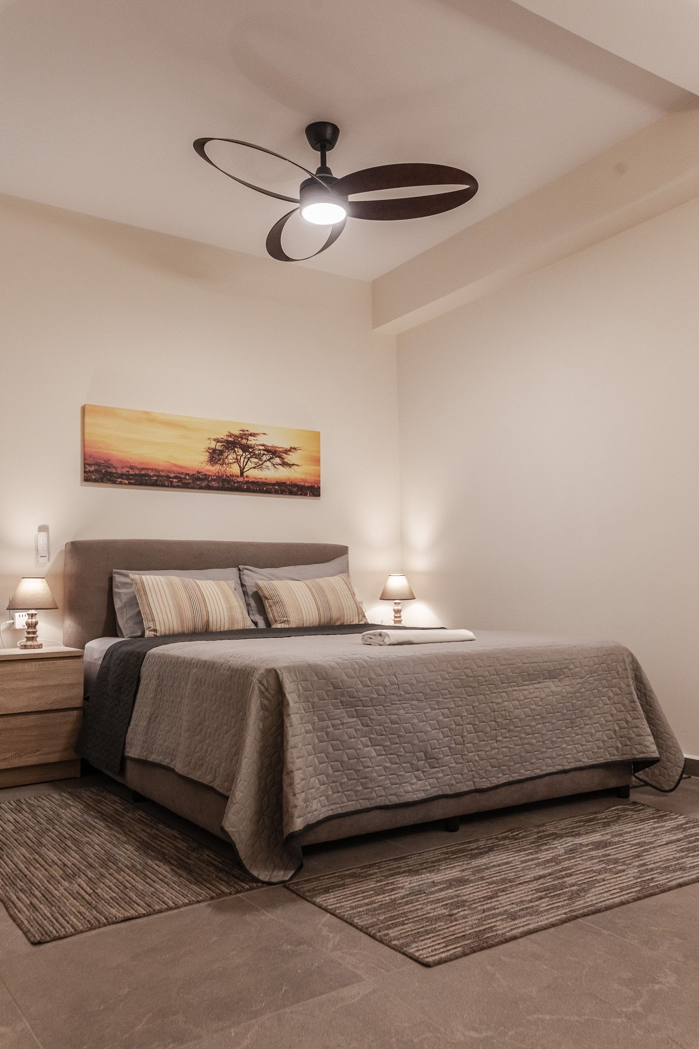 Cozy bedroom with a bed, bedside lamps, ceiling fan, and neutral decor in beige tones